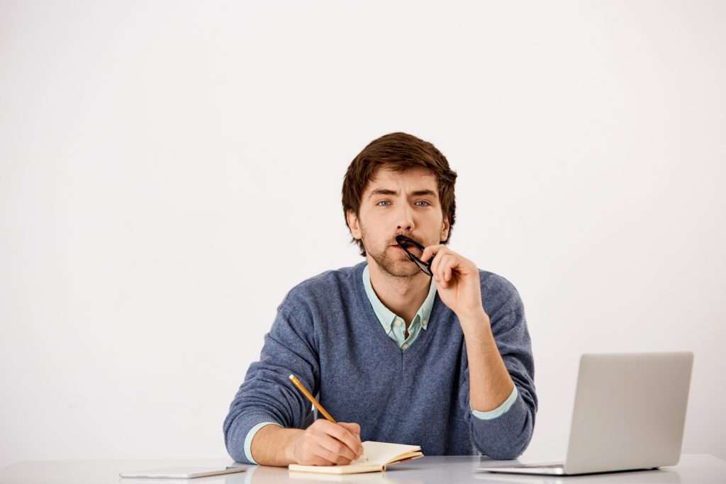 thoughtful businessman sitting office desk writing trying think up idea squinting as pondering new content